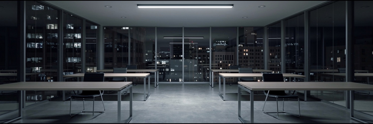 An empty glass-walled office floor at night with bare desks and no people